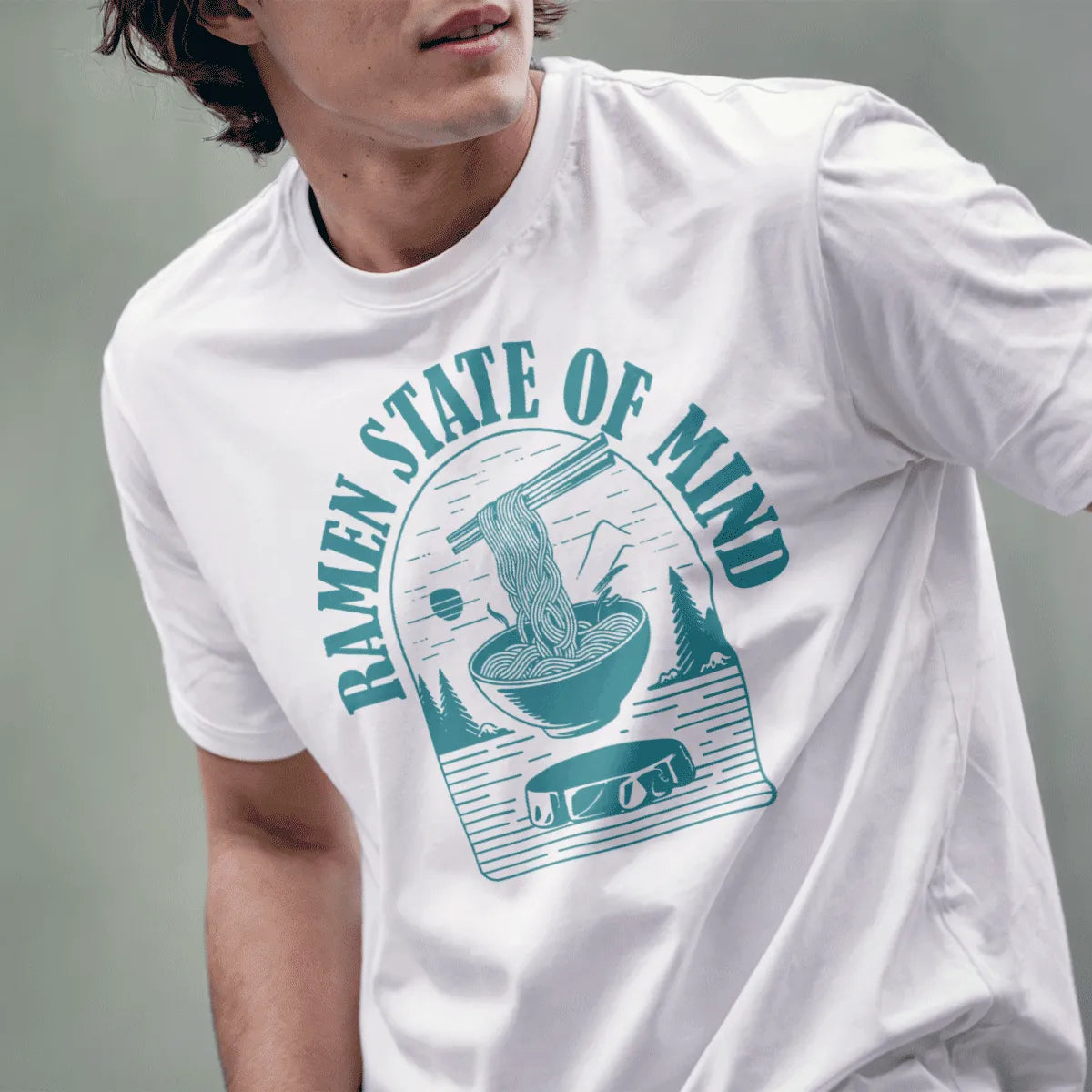 Male model wearing white t-shirt with teal ramen bowl, pine trees, and mountain, ramen t-shirt, motivational quote.
