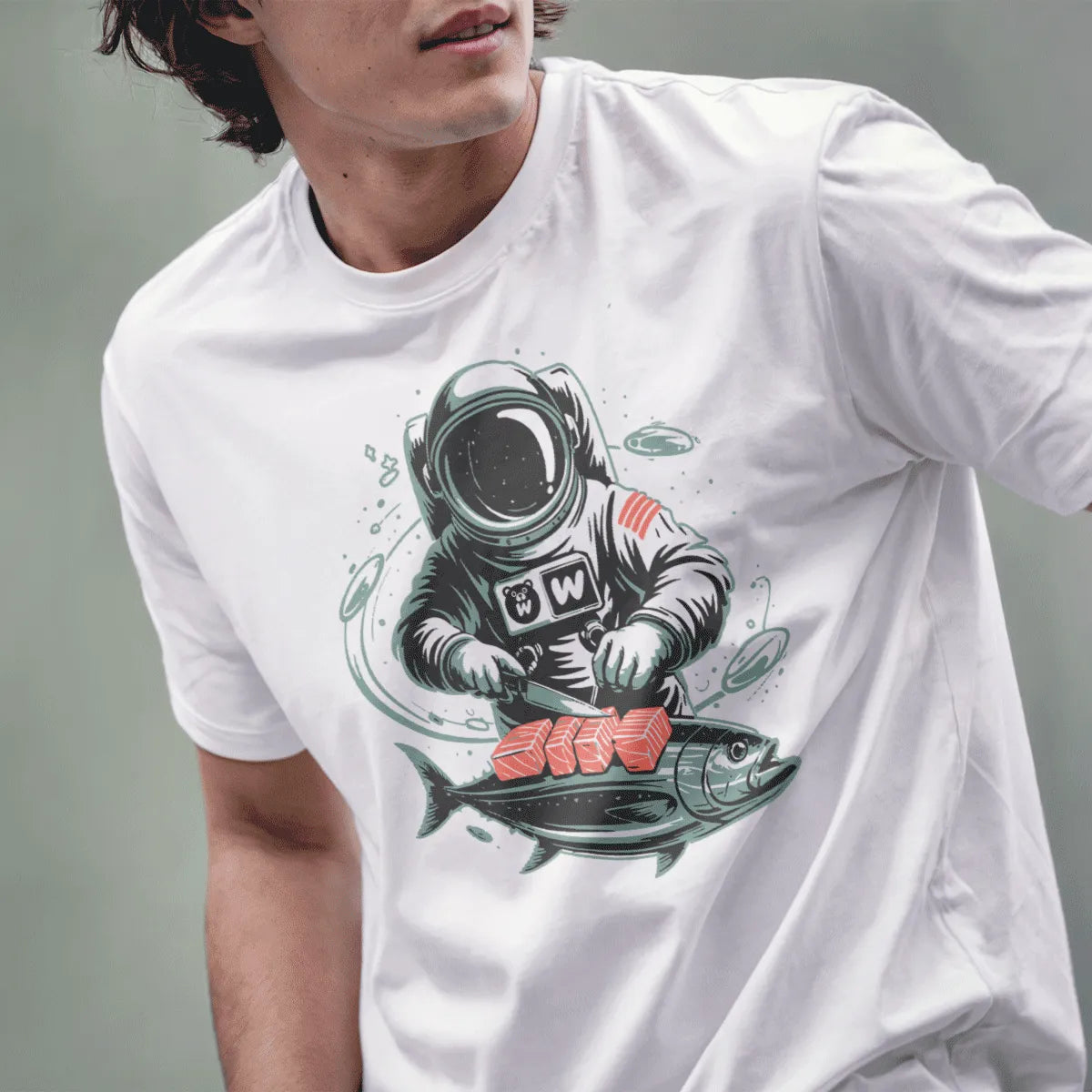 Male model wearing white Japanese t-shirt with whimsical astronaut preparing sushi illustration.