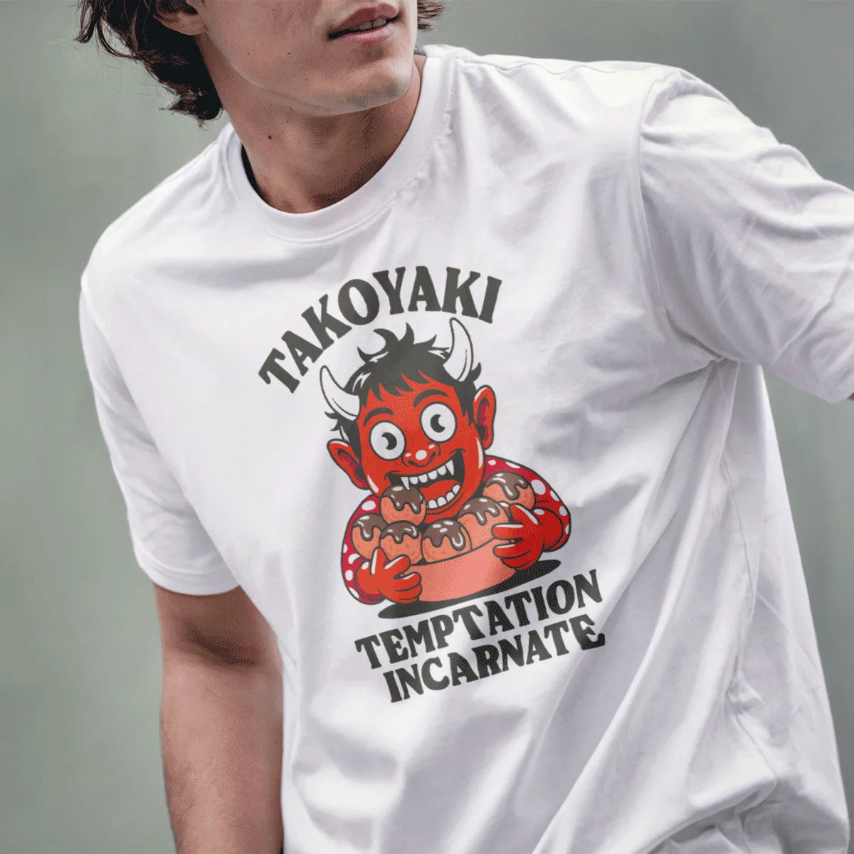Male model wearing white t-shirt with cartoonish red oni holding Japanese snack popular takoyaki.