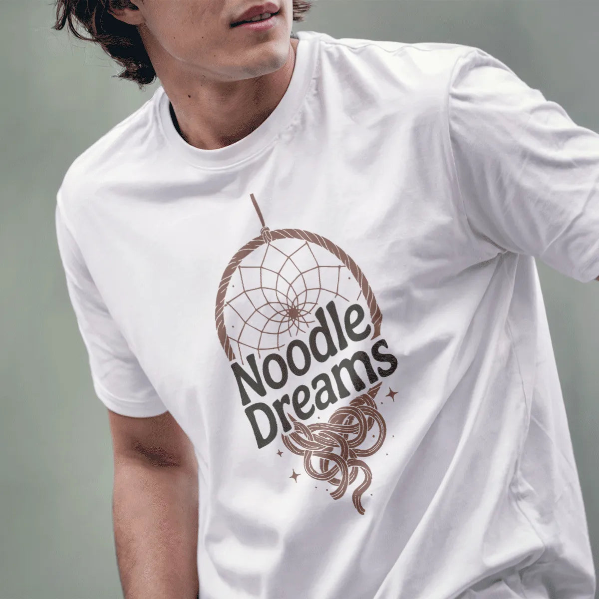 Male model wearing white t-shirt with folk art dreamcatcher design and "Noodle Dreams" text.