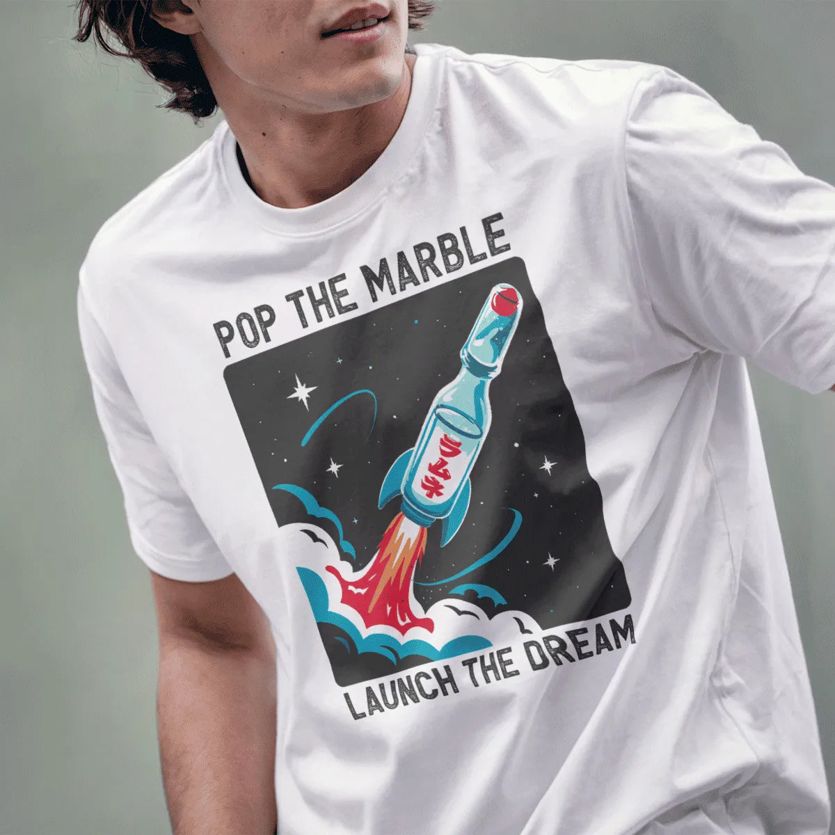 Male model wearing white t-shirt with whimsical Ramune bottle spaceship and "Pop the Marble" text.