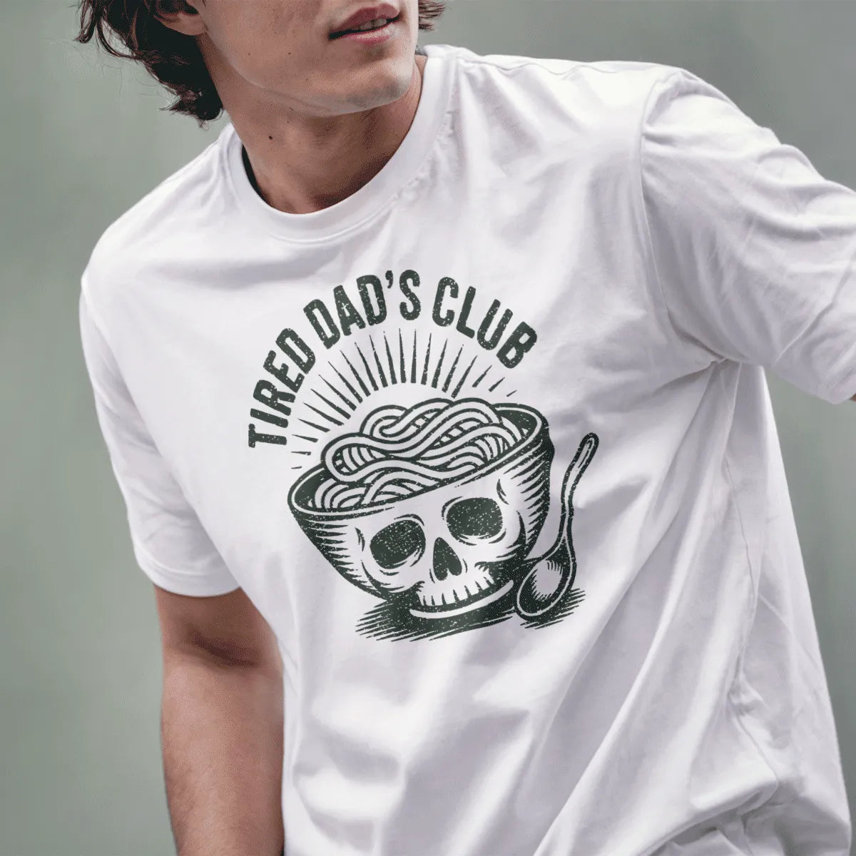 Male model wears white tee with graphic ramen bowl skull and gritty distressed text, hands visible.