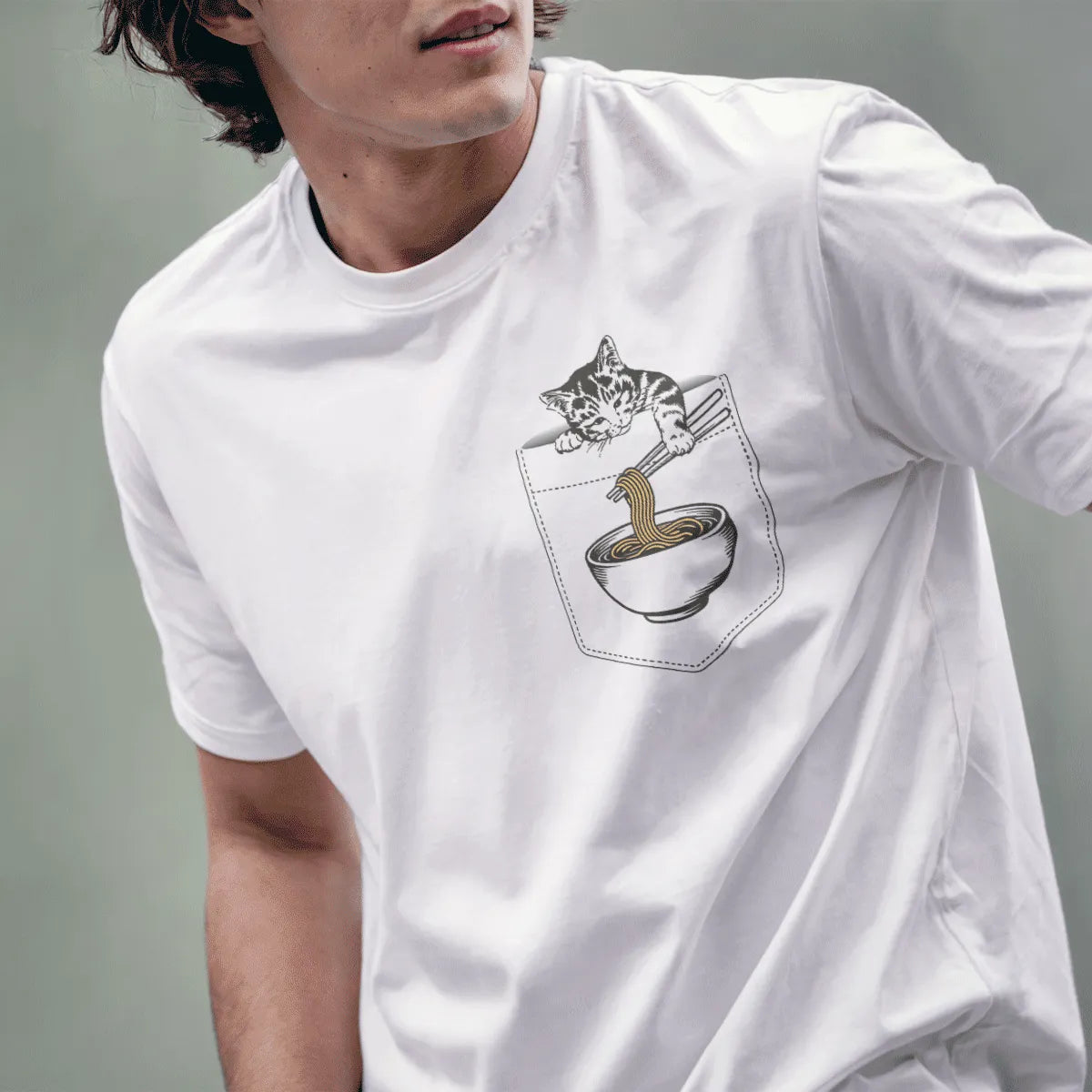 Male model wearing white tee with playful tabby peeking from faux denim pocket, holding ramen and chopsticks.