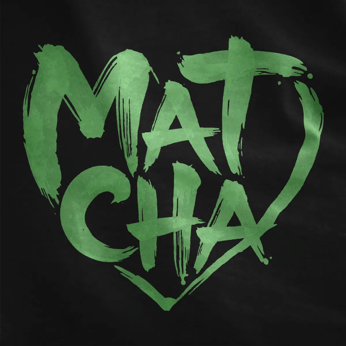 Green brushstroke "Matcha" heart with textured, hand-painted script on black fabric close-up.