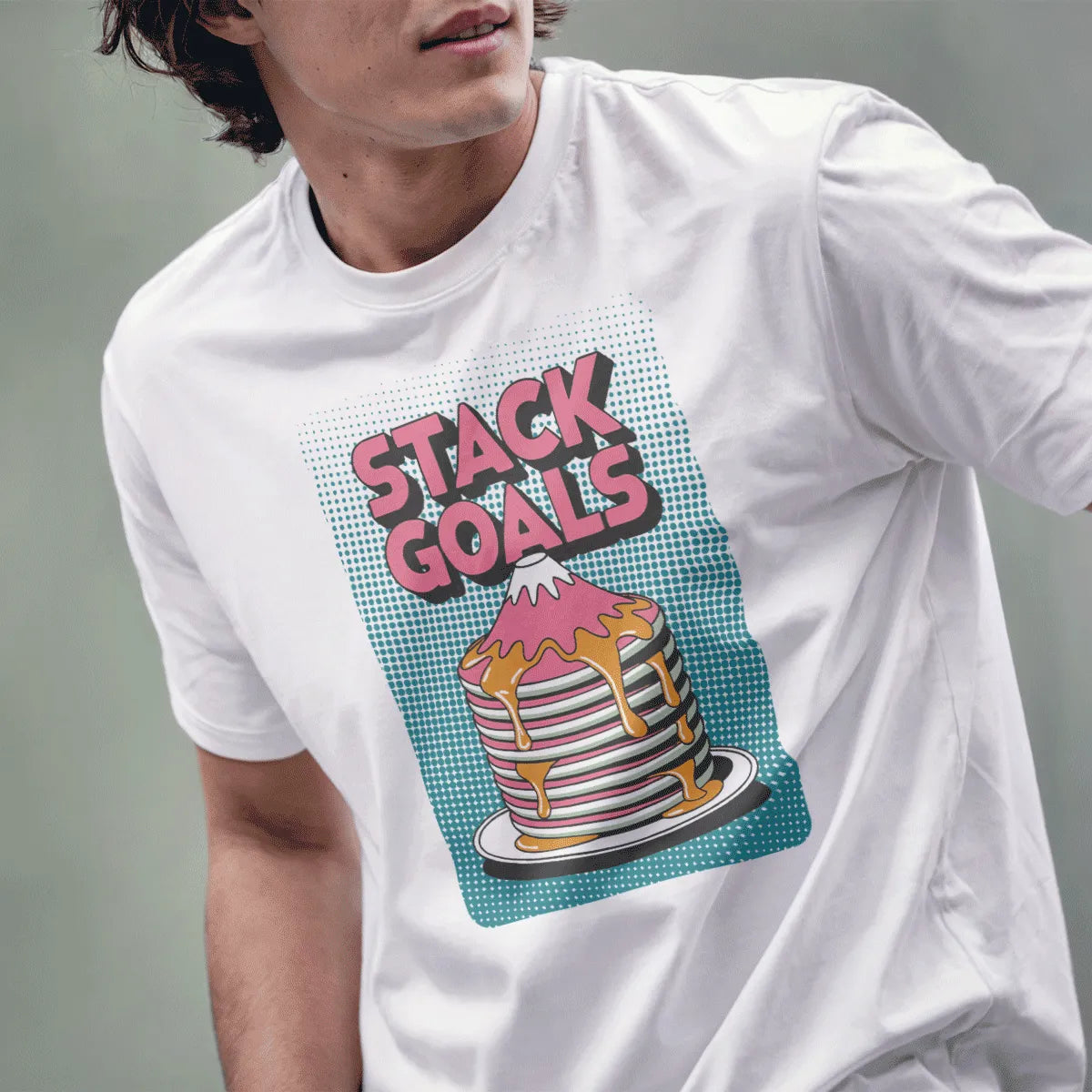 Male model wearing white tee with retro pink "STACK GOALS" text above pancake mountain shaped like Mount Fuji.