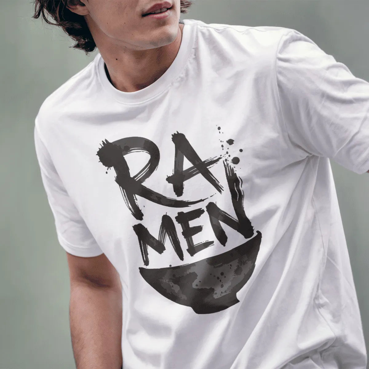 Male model wearing white t-shirt with bold brushstroke "RAMEN" text and textured ramen bowl design.