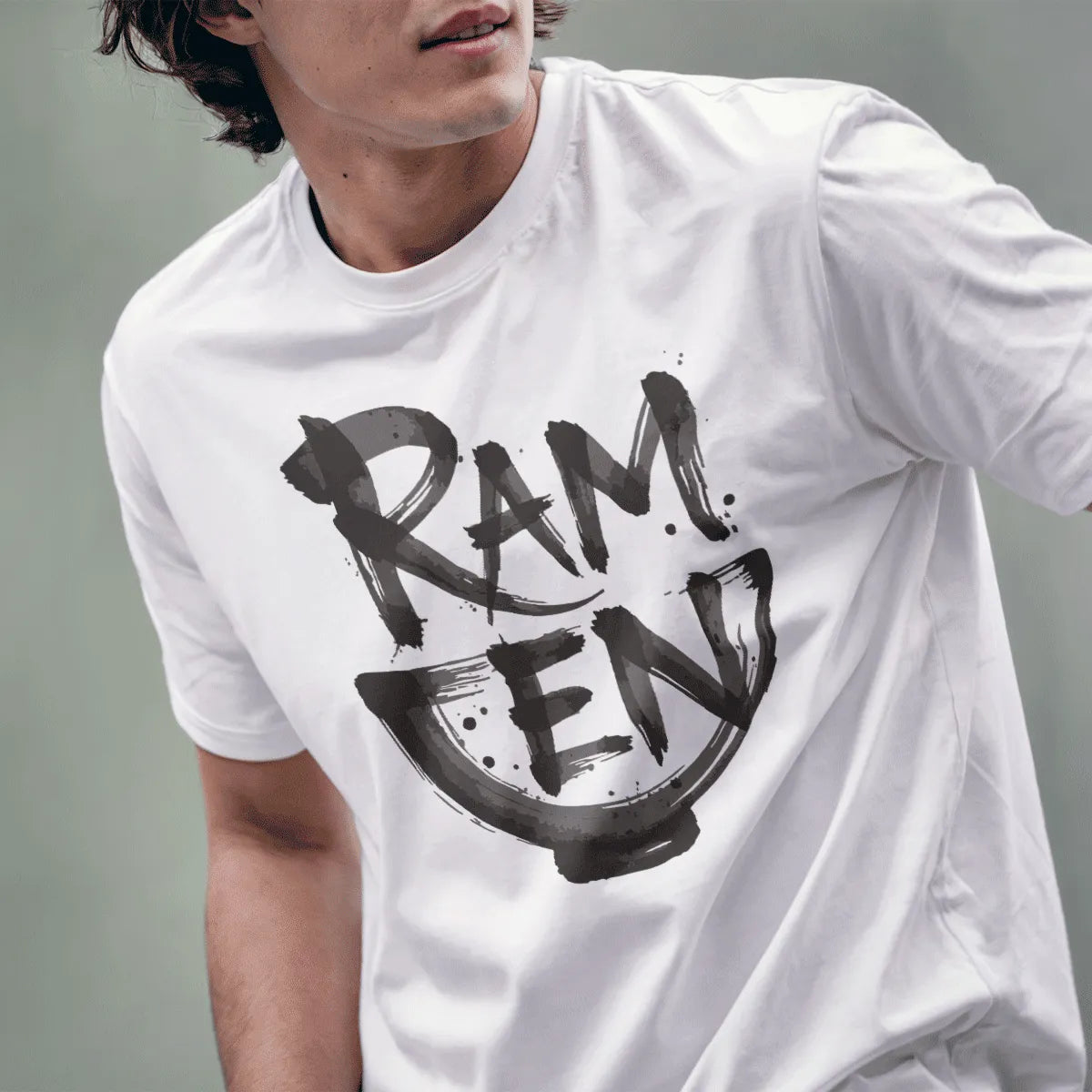 Male model wearing white t-shirt featuring dynamic brushstroke ramen text forming bowl shape in monochrome style.