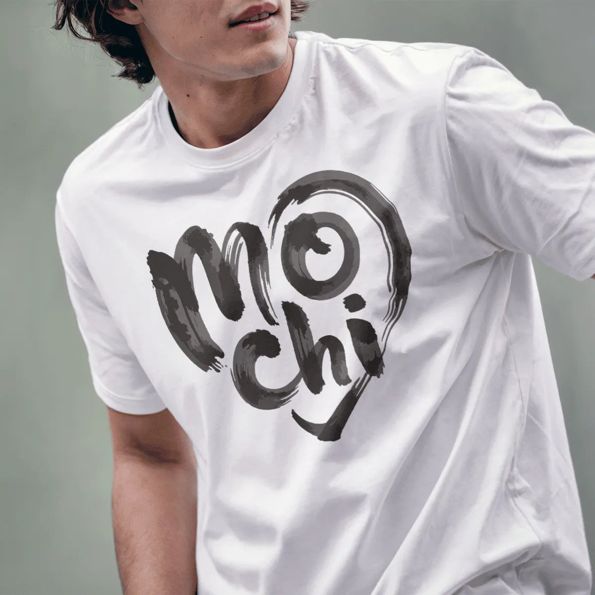 Male model wearing white t-shirt featuring expressive mochi text in brushstroke style inside heart outline.