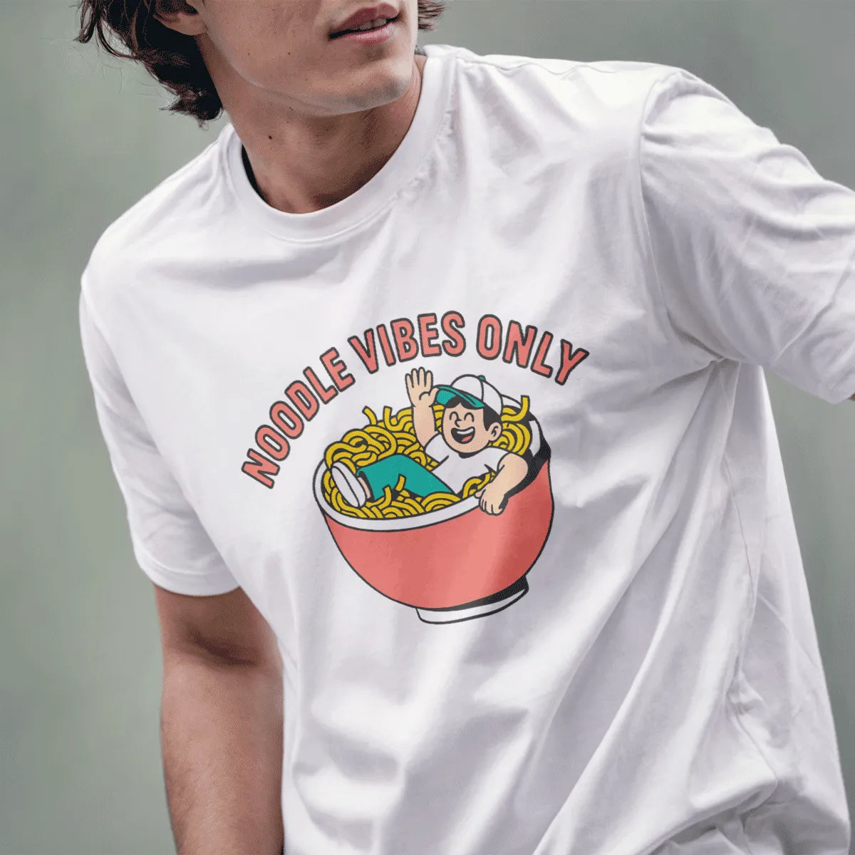 Male model wearing white tee with playful ramen bowl and waving figure in bright, cartoon style.