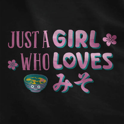 Black closeup of kawaii clothes design with pink and teal text, sakura flowers, and cute miso soup bowl.