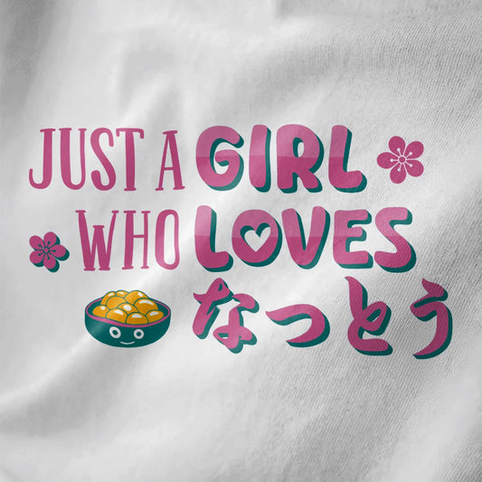 White fabric close-up of kawaii natto bowl, pink cherry blossoms, and playful slogan on t shirt design graphic.