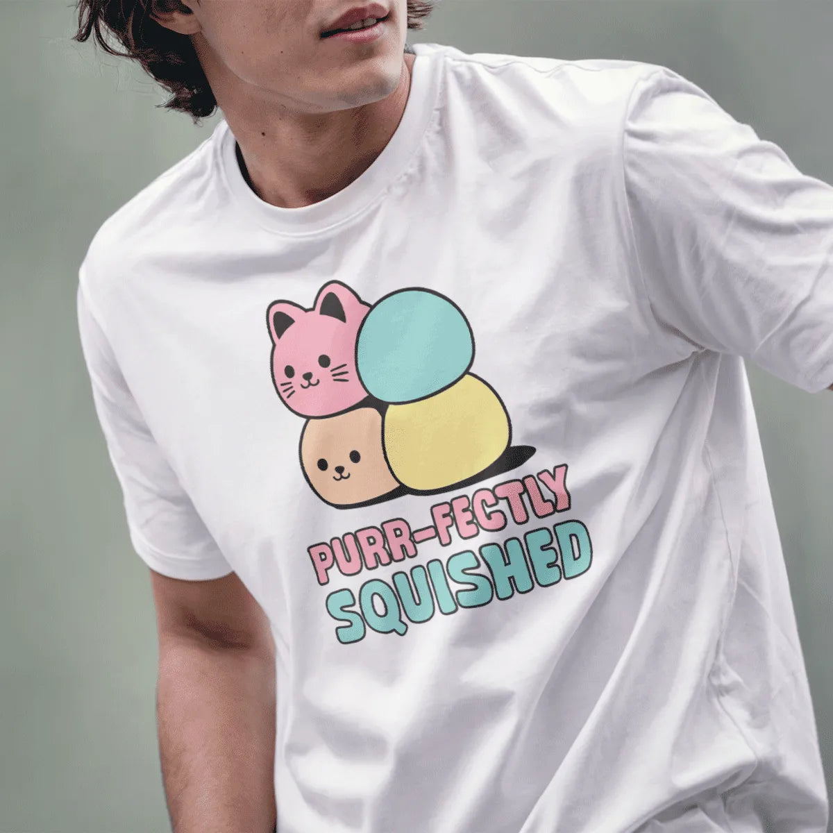 Male model in white t-shirt, two mochi cats, playful "PURR-FECTLY SQUISHED" text, funny cat shirt, whimsical illustration.